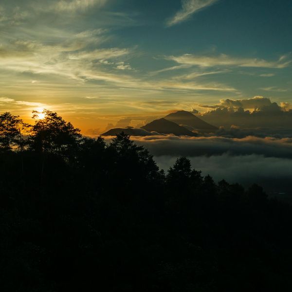 Silhouette of a person dancing against a sunrise with mint green hues.